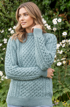 Woman wearing a teal knitted sweater standing in front of green foliage and white flowers