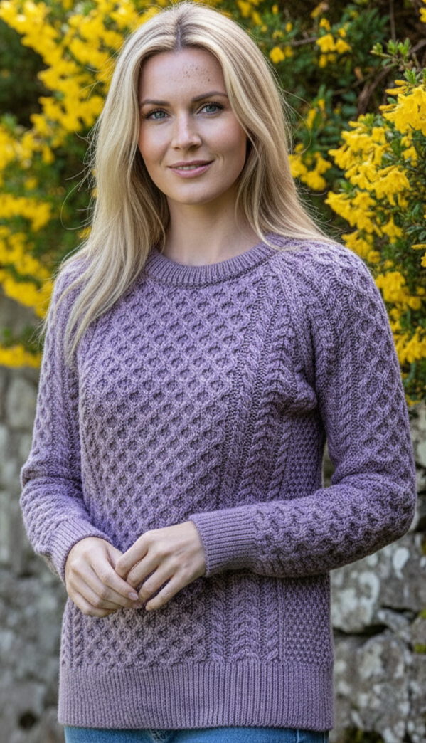 Woman wearing a purple sweater standing in front of a stone wall and yellow flowers
