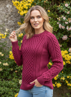 Woman wearing a maroon knitted sweater in a garden setting with flowers and a stone wall.
