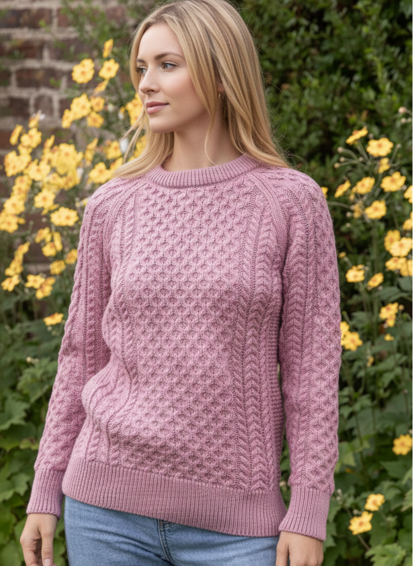 Woman wearing a pink knitted sweater standing in front of a brick wall and greenery.
